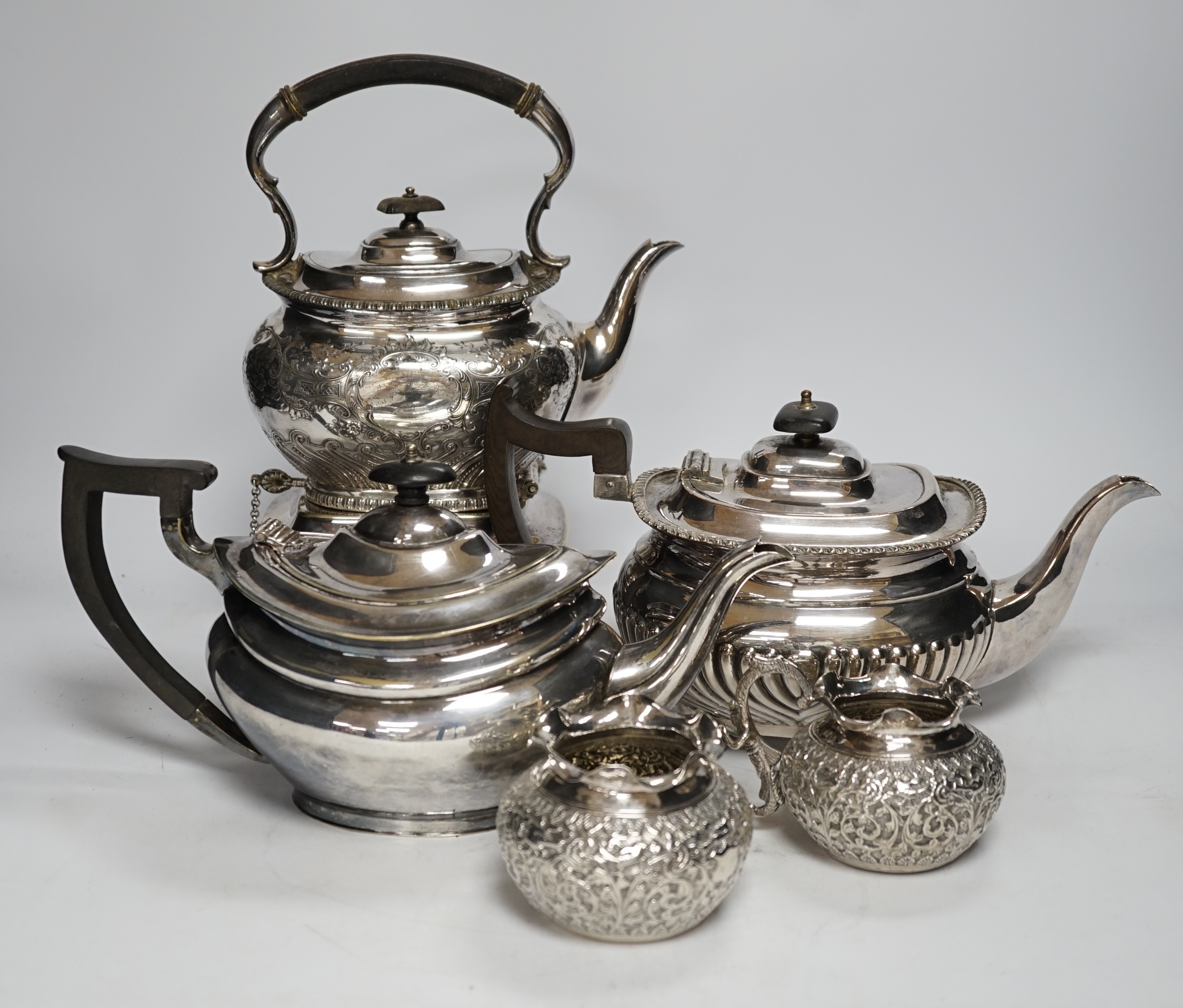 A plated kettle on stand, two plated teapots, a sugar bowl and a cream jug